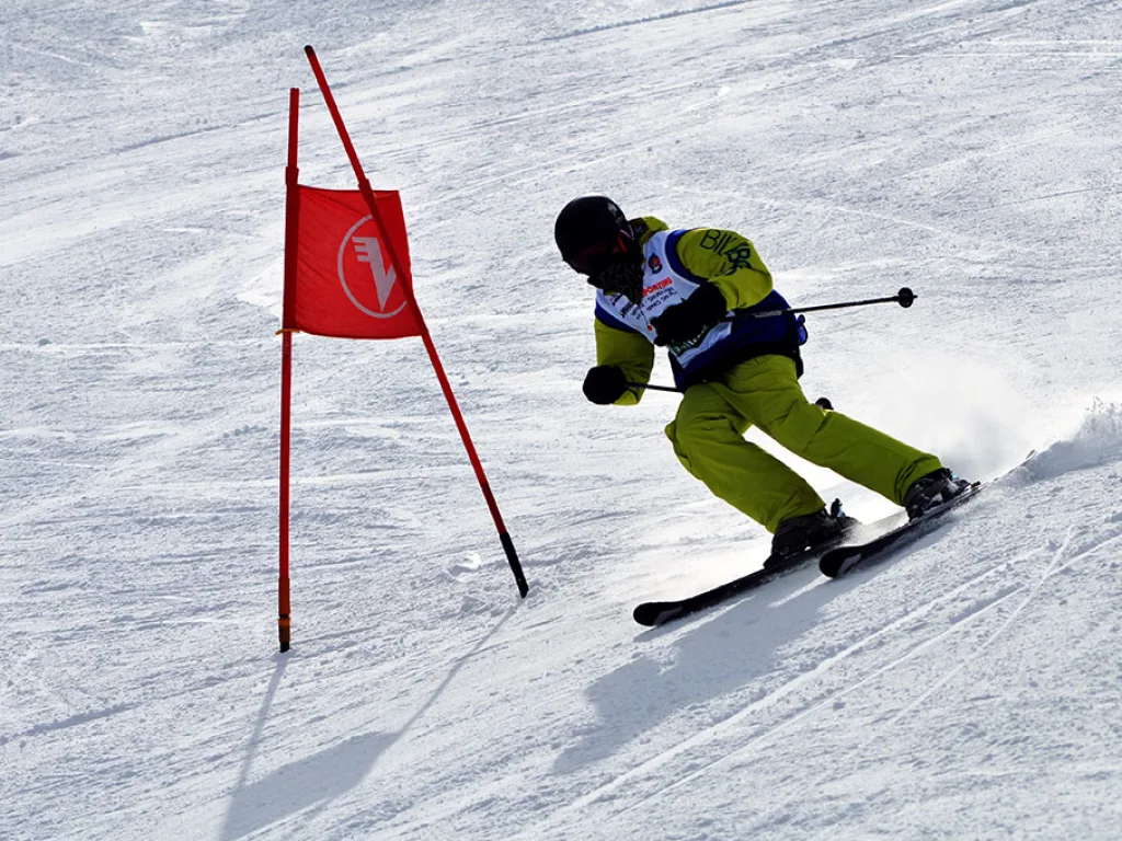 Skifahrer in gelber Hose umfährt ein rotes Tor.